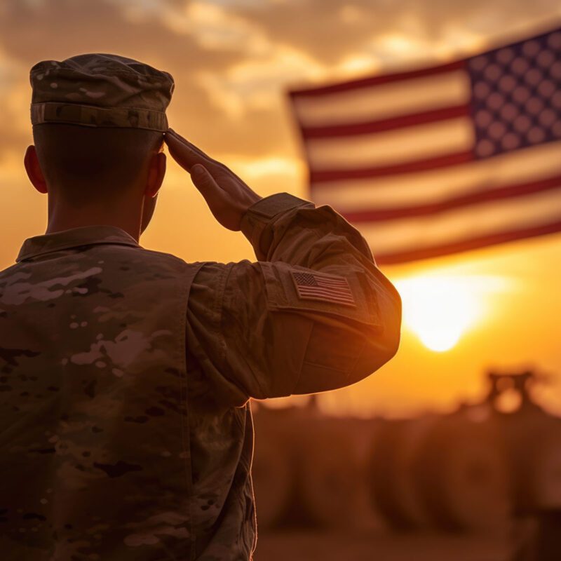 veteran saluting the American flag while the sun sets in the background.