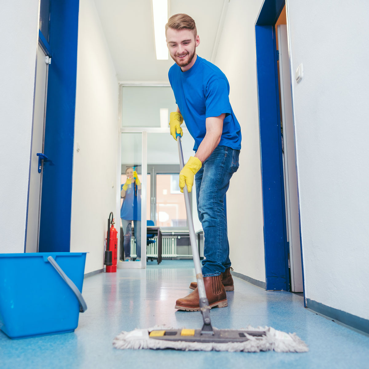 Man mopping a hallway wearing a blue t-shirt.