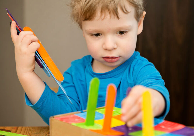 Young boy playing with toy made from cardboard box and ice-cream sticks