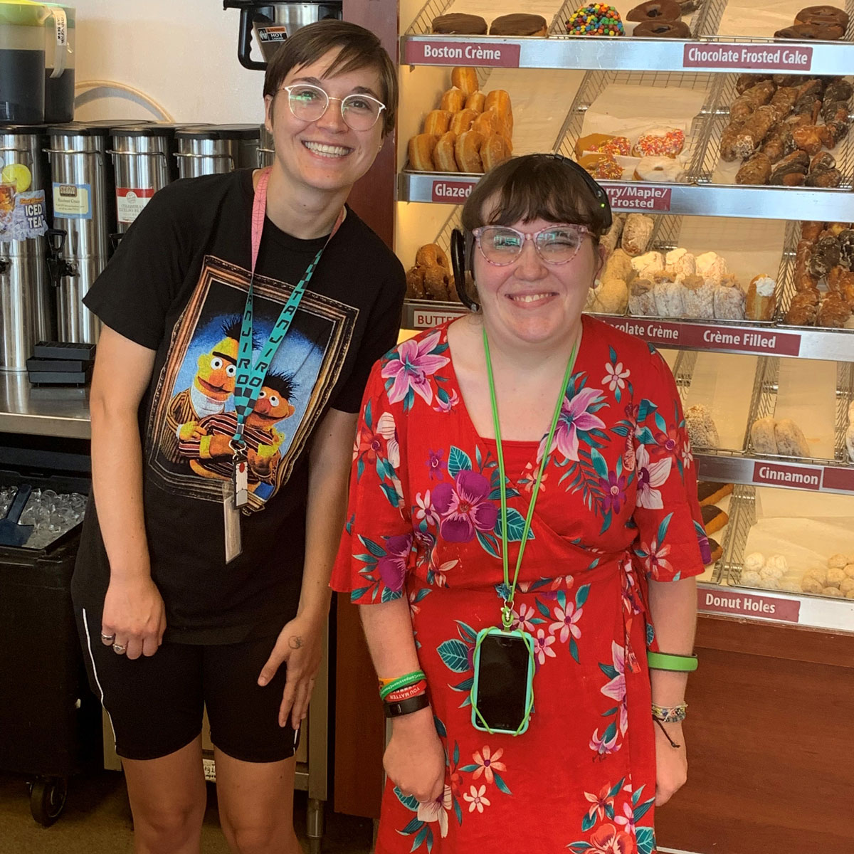 Mikayla and Leslie smiling for a photo in front of the donut shelf at Dunkin Donuts