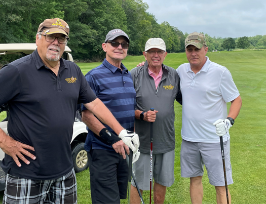 Four men standing on a golf course and smiling at the camers