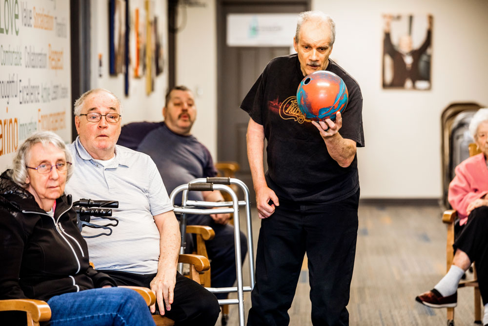 An old man getting ready to throw his bowling ball as other people look on.