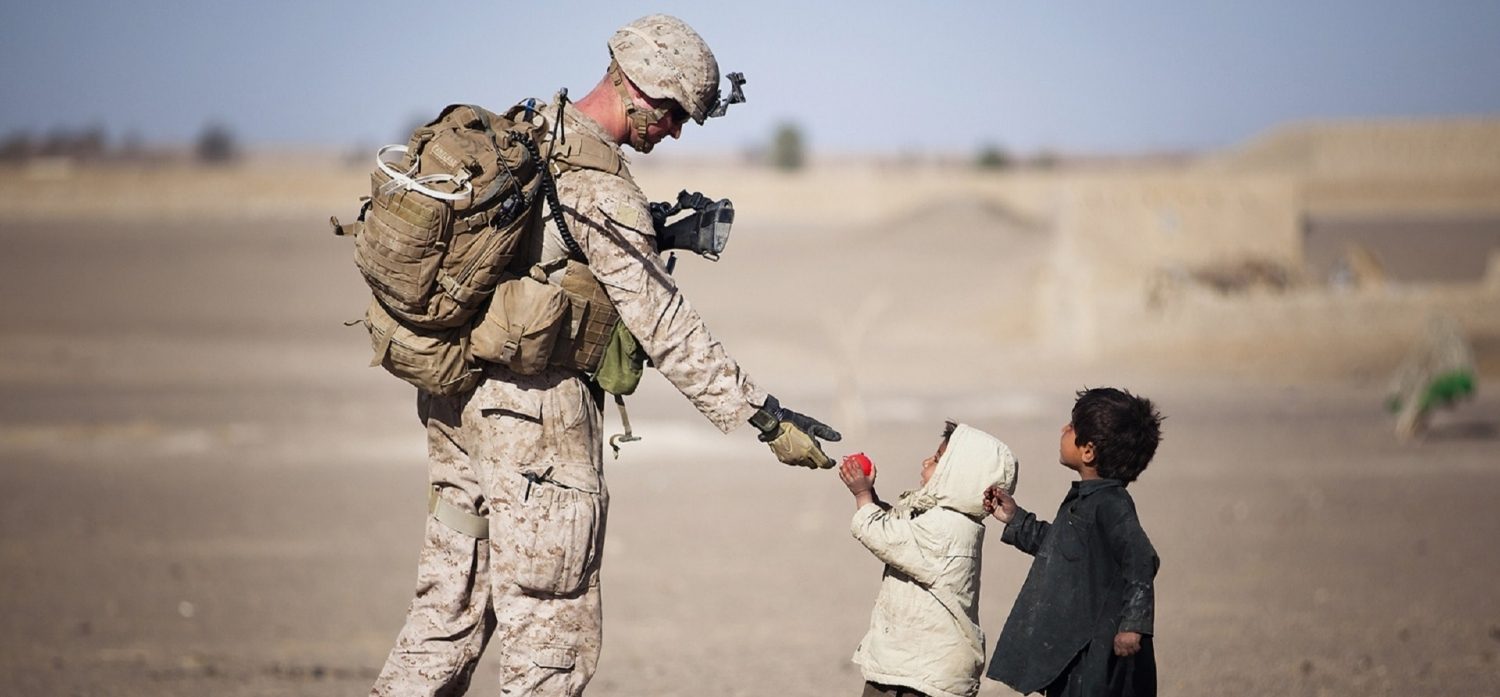 A deployed United States Marine giving children food in the desert.