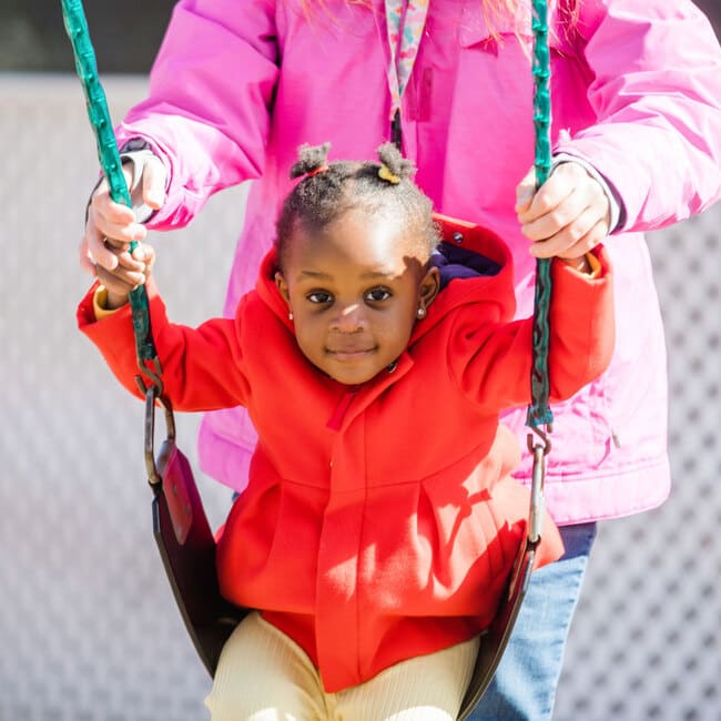 Young girl on swing set wearing a red jacket.