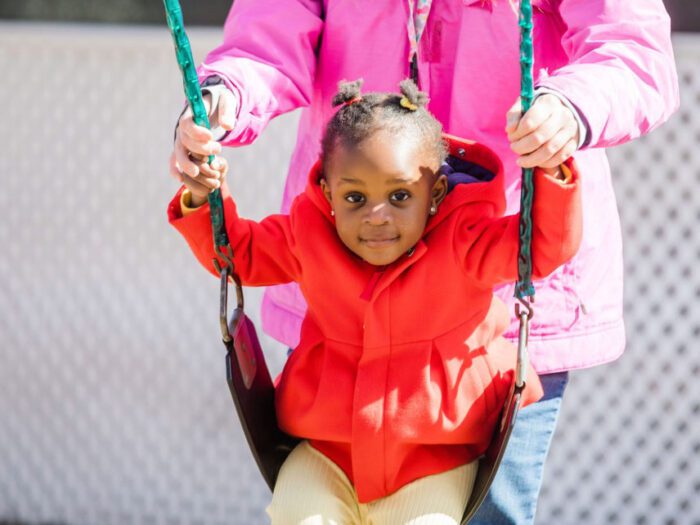 Young girl on swing set wearing a red jacket.
