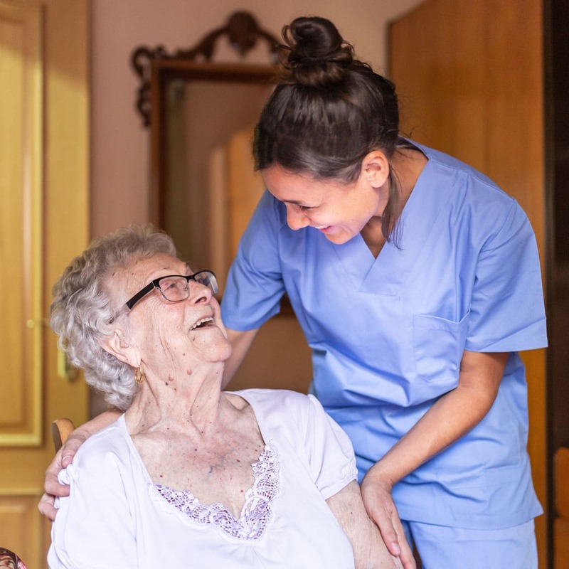 In home healthcare nurse and older woman smiling at each other.