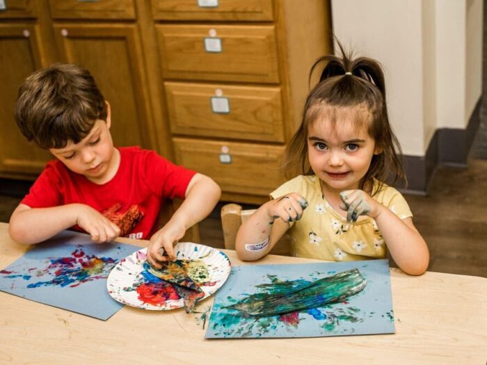 Girl and boy finger painting in school classroom. 