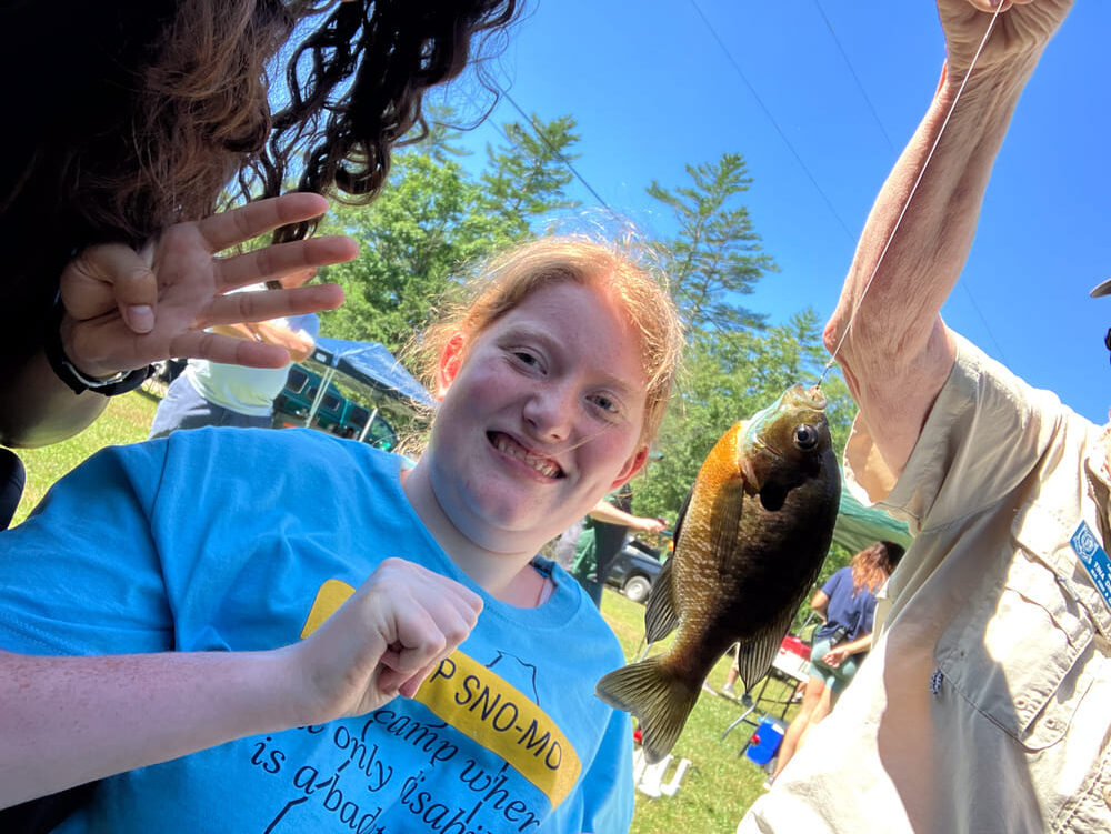 Girl looking at a small fish on a hook at the 2024 Camp Sno Mo fishing derby