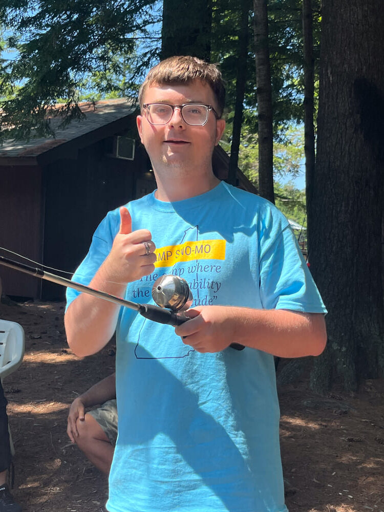 Boy holding a fishing rod and giving a thumbs up at the 2024 Camp Sno Mo fishing derby