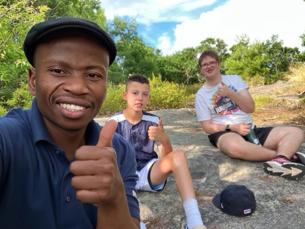 Three boys sitting on a large rock giving the thumbs up at Camp Sno Mo.