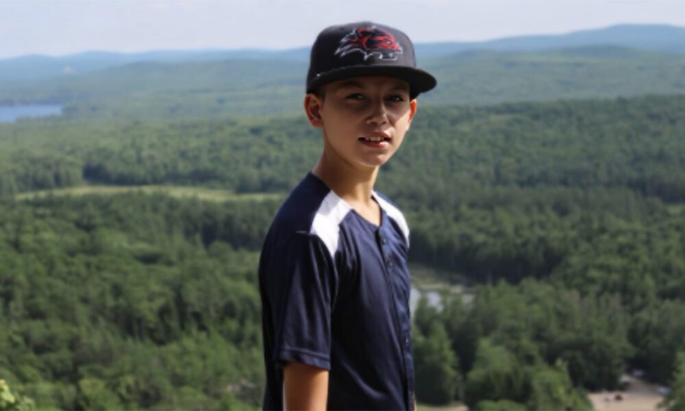 Boy wearing blue shirt and hat with mountains in the background