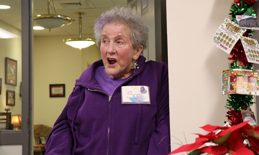 A woman wearing a purple sweater with a name tag on that reads, "Sooz".