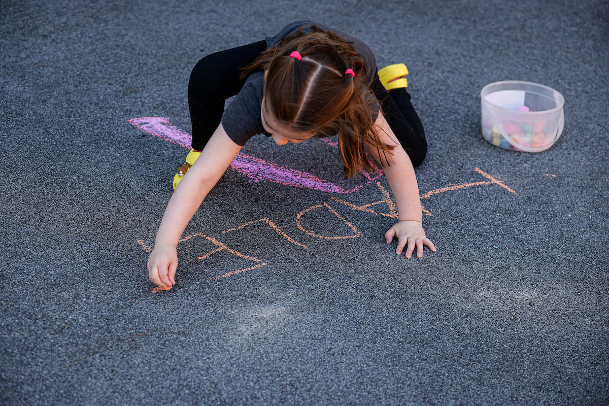 Child drawing on a driveway with orange chalk.
