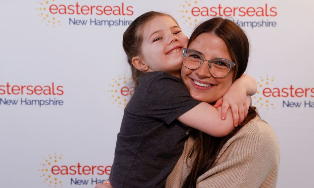 Mother holding daughter in front of an Easterseals New Hampshire step and repeat background