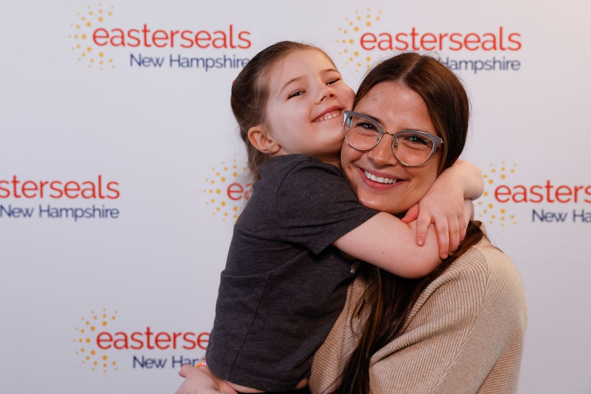 Mother holding daughter in front of an Easterseals New Hampshire step and repeat background