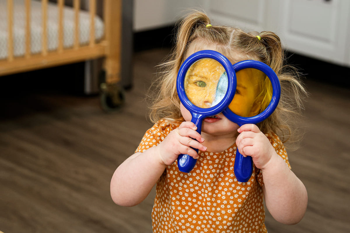 Young girl wearing orange shirt holding magnifier glass.