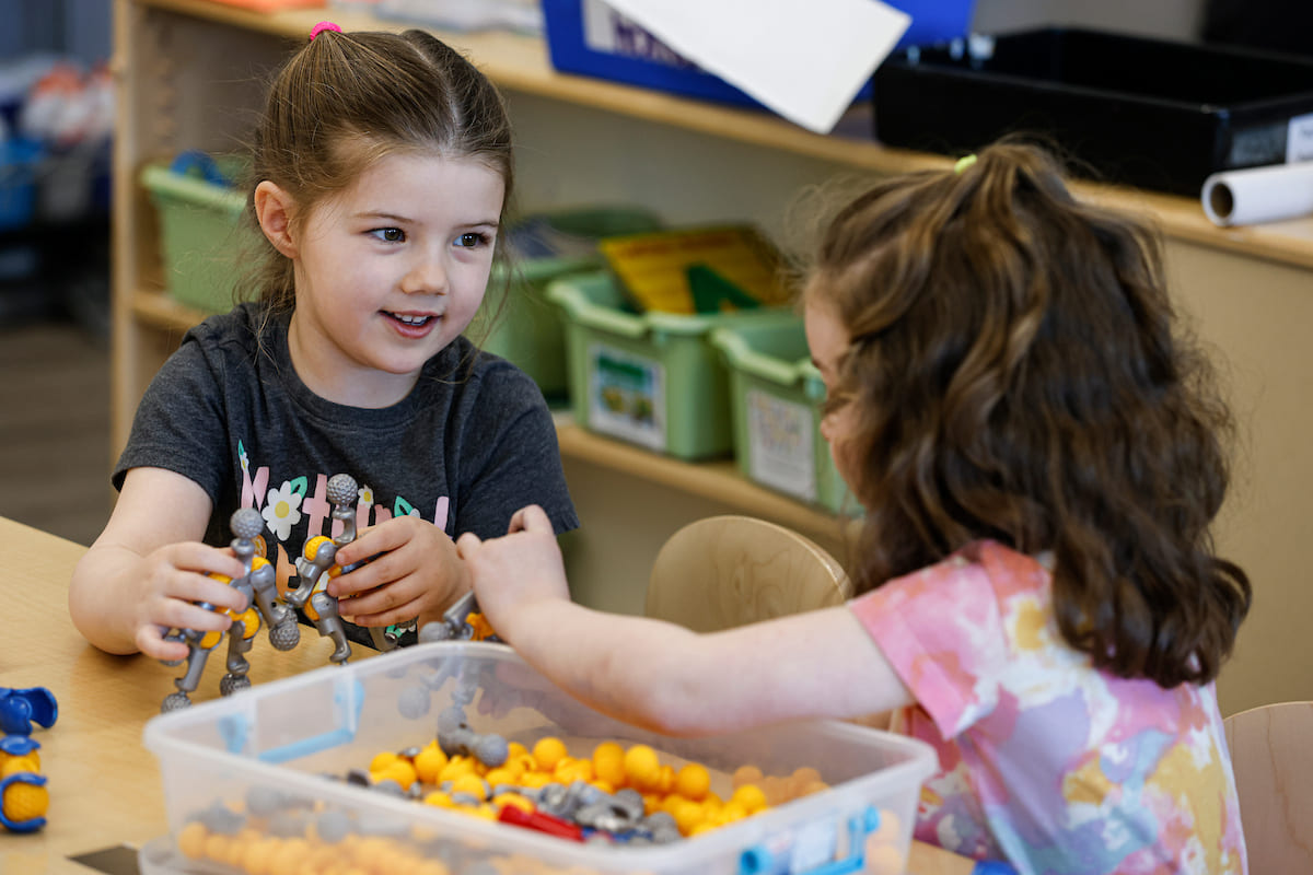 Two young girls playing with toys inside of a classroom