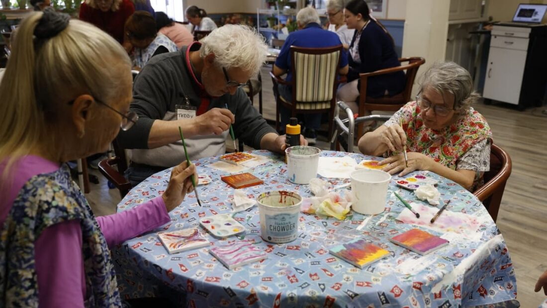 3 adult day participants painting at a table