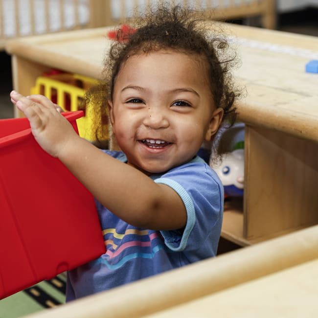 Child holding red bin in classroom