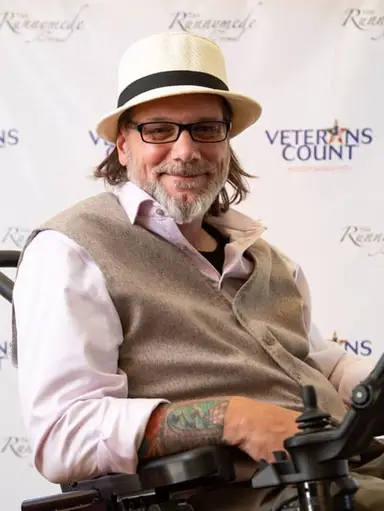 Man in wheel chain with Veterans Count step and repeat banner in the background.