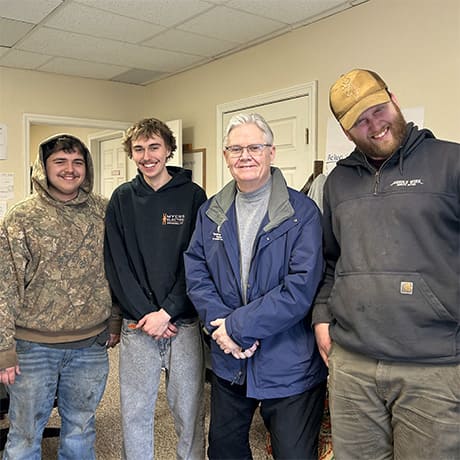 Group photo of four men in an office with tan walls